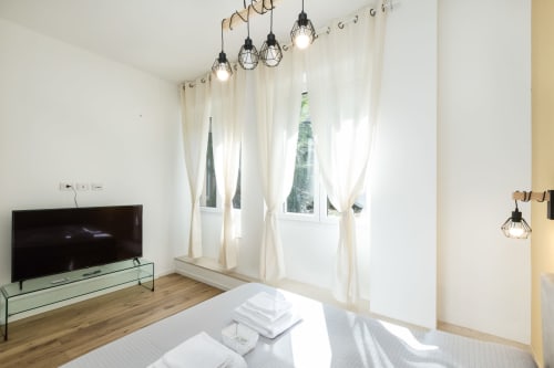 Modernes Schlafzimmer im Magnolia Apartments Milan mit Pendelleuchten, Flachbildfernseher, cremefarbenen Vorhängen, Holzböden und Garten