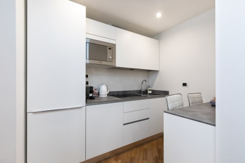 Moderne weiße Küche mit schwarzen Arbeitsplatten, Mikrowelle und Essbereich in den Magnolia Apartments Milan