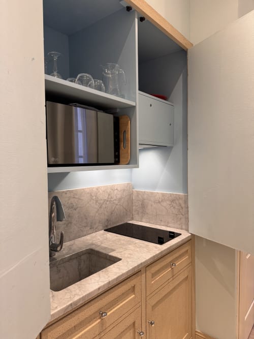Modern kitchenette in O Pitchoun apartment at Mes à Moi Pézenas with marble countertop, wooden cabinets, and wall-mounted TV
