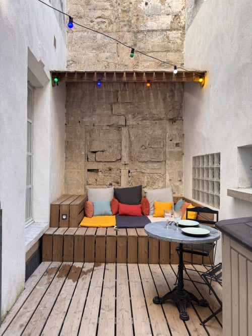 Cozy inner courtyard patio at Mes à Moi Pézenas with colorful cushions, wooden seating, bistro table, and string lights