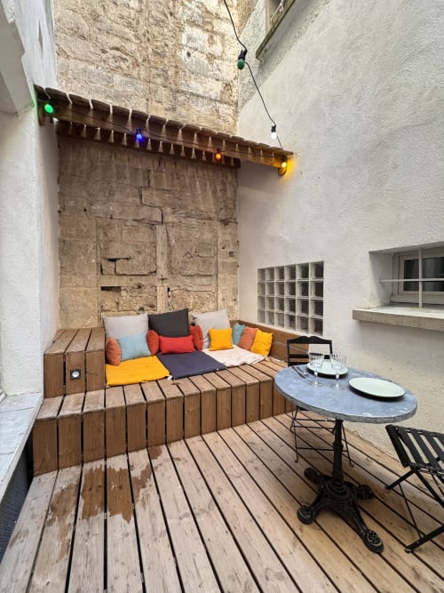 Cozy inner courtyard patio at Mes à Moi Pézenas with wooden seating, colorful cushions, and dining setup