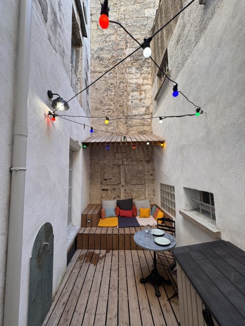 Cozy inner courtyard patio at Mes à Moi Pézenas with colorful string lights, wooden deck, cushioned seating, and dining