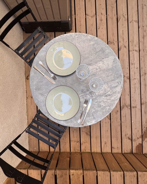 Overhead view of two place settings on round stone table at Mes à Moi Pézenas, with black chairs and wooden deck