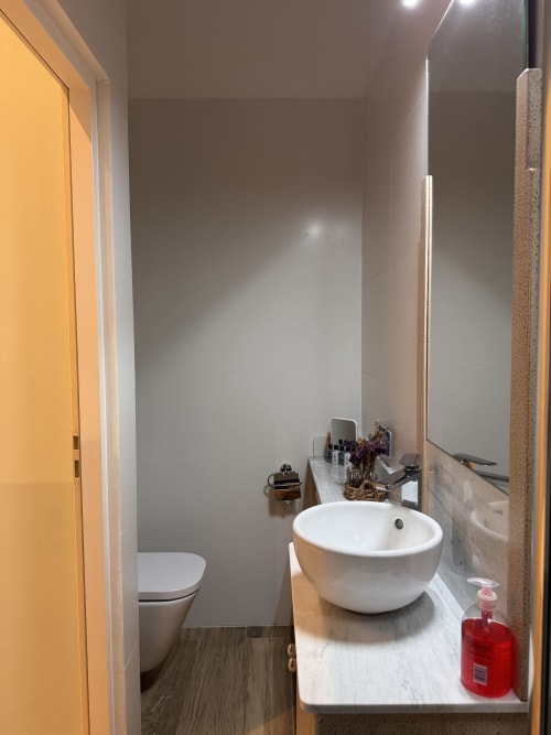 Modern bathroom with white round vessel sink, toilet, grey tile walls, and yellow door at Mes à Moi Pézenas BnB