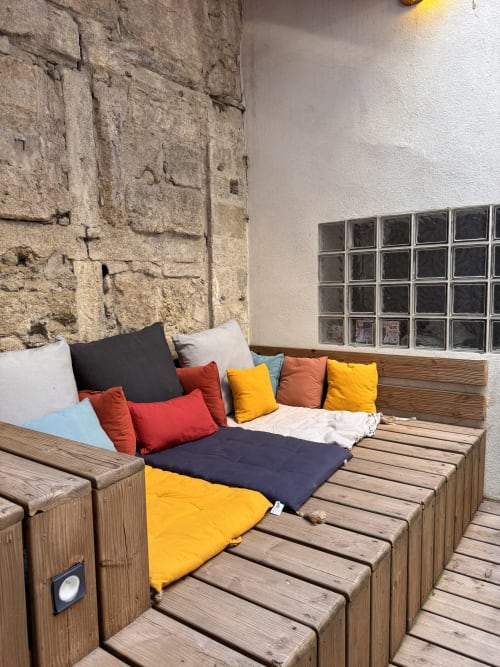 Colorful cushioned seating on wooden deck with stone walls at Mes à Moi Pézenas apartment