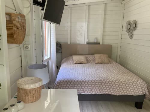 Chambre lumineuse aux Villas aux Antilles avec lit queen-size, murs blancs en bois, TV, ventilateurs et vue sur le jardin