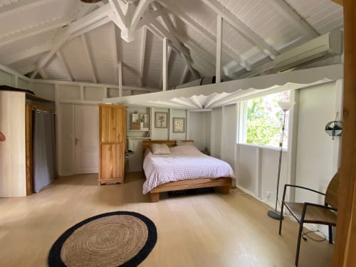 Chambre spacieuse aux Villas aux Antilles avec lit en bois, plafond à poutres apparentes, vue sur le jardin et équipements modernes