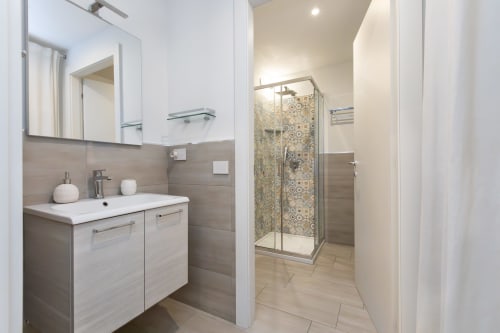Modernes Badezimmer in der Magnolia Apartments Milan mit Waschbecken, Spiegel und begehbarer Dusche mit dekorativen Fliesen