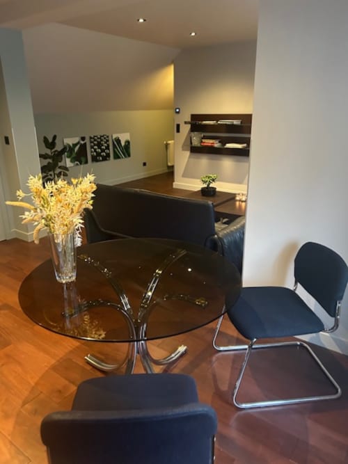 Modern dining area with round glass table, black chairs, and yellow flowers at Le Petit Château apartment in Baye, France