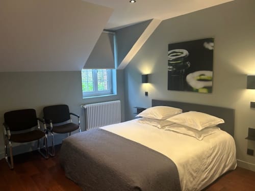 Modern attic bedroom at Le Petit Château with queen bed, cream pillows, dark gray bedding, angled ceiling, window with garden