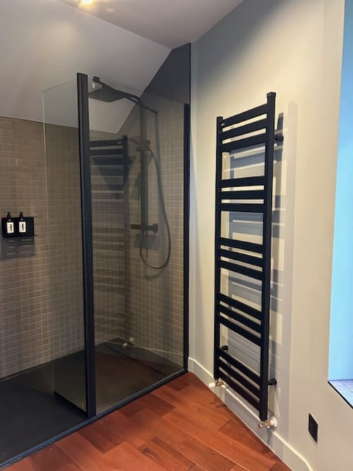Modern black-framed shower enclosure with heated towel rail in Le Petit Château apartment bathroom, Baye