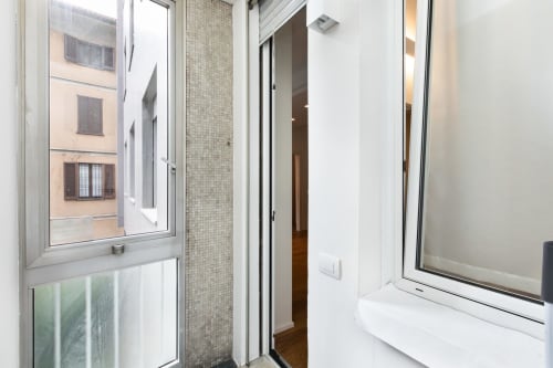 Moderner Apartmentkorridor mit gekacheltem Badezimmereingang, weißen Türen und Fenster mit Blick auf Mailänder Innenhof im Magnolia