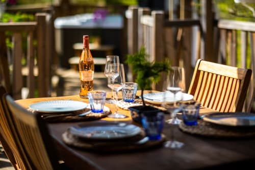Table de salle à manger en plein air à Domaine De Campagnac avec bouteille de vin, couverts et chaises en bois à Carsac-Aillac