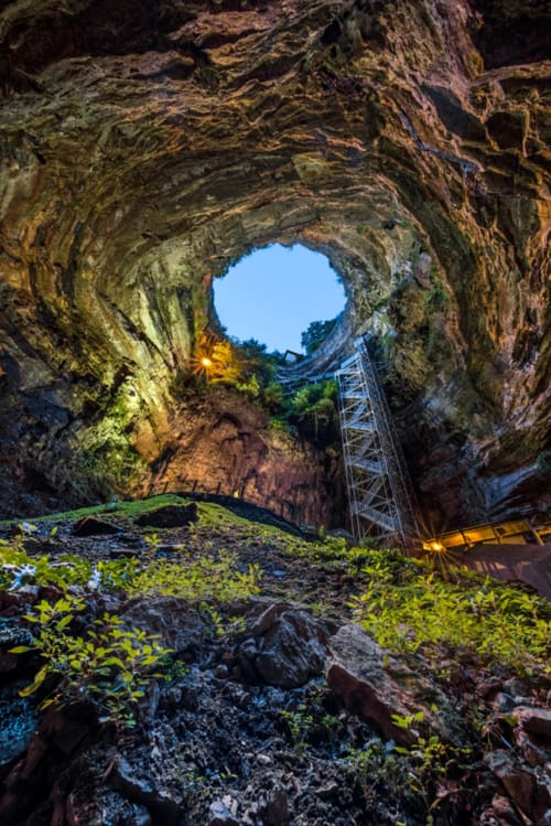 Underground cave with natural opening at Domaine De Campagnac, Carsac-Aillac, showing moss-covered rocks and metal staircase