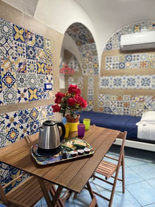 Camera in stile mediterraneo presso la San Nicola Suite a Sorrento con decorazioni in maiolica, tavolo in legno, rose rosse e volta ad arco