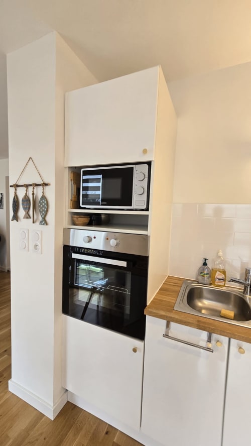 Modern kitchen corner in Ô KASTEL apartment with white cabinetry, built-in microwave, oven, wooden countertop, and stainless