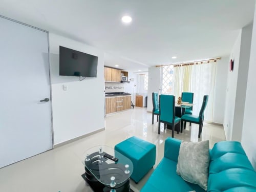 Apartamento moderno en Olamar Living con asientos turquesa, cocina, comedor y TV en Santiago de Tolú, Colombia