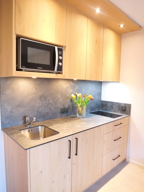 Kitchenette moderne avec armoires en bois clair, évier en acier inoxydable et micro-ondes à l'Hôtel Studios La Rochetaillée