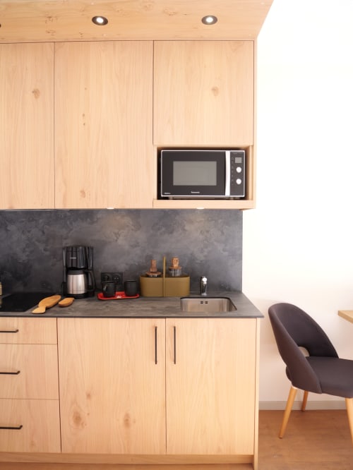 Kitchenette moderne avec meubles en bois clair, micro-ondes et plan de travail foncé aux Studios La Rochetaillée