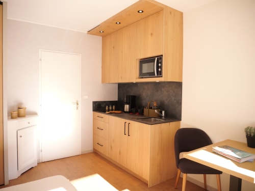 Kitchenette studio avec meubles en bois, plan de travail noir et coin repas à l'Hôtel Studios La Rochetaillée