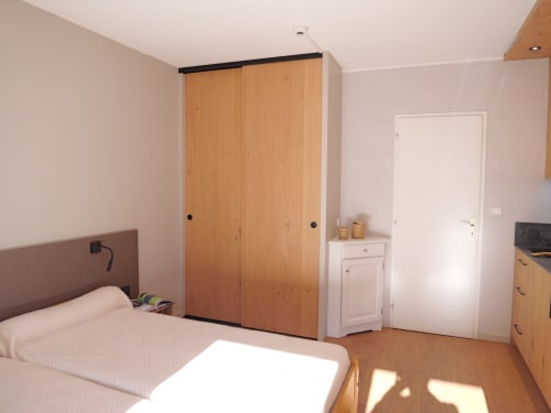 Chambre lumineuse aux Studios Hôtel La Rochetaillée avec armoire en bois, lit, porte blanche et vue sur les montagnes