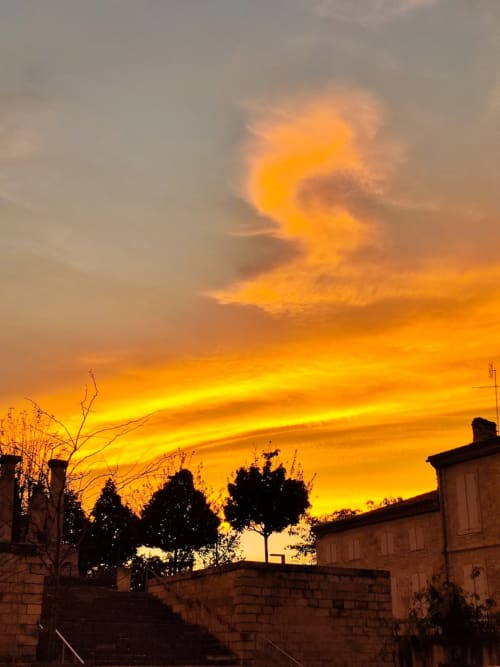 Dramatic orange sunset over Le Rêve d'Alice in Saint-Puy, France, silhouetting historic stone buildings and trees