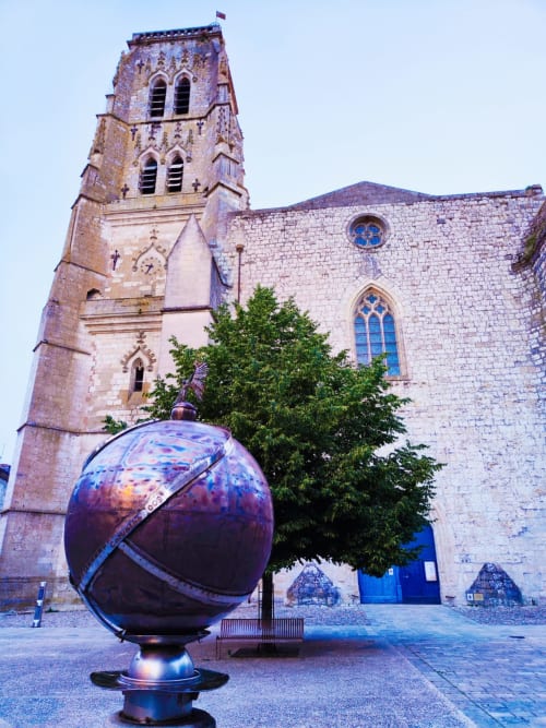 Medieval stone church with bell tower at Le Rêve d'Alice BnB in Saint-Puy, France, featuring blue-striped metal sphere