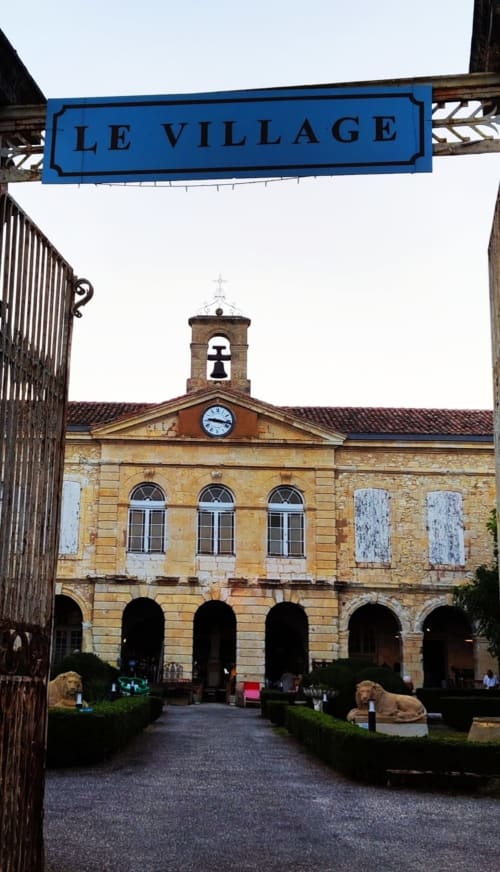 Le Village sign above a historic stone building with bell tower and courtyard at Le Rêve d'Alice B&B in Saint-Puy, France