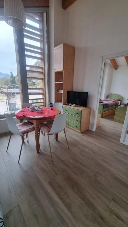 Moderno appartamento a Maso Kreuzberg a Trento con tavolo da pranzo, arredamento in legno, letto verde e vista sulle montagne