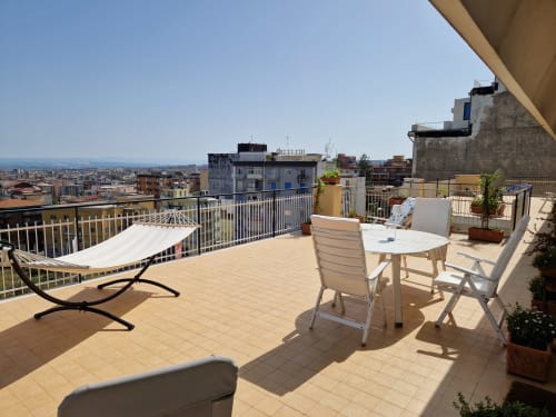 Soleggiata terrazza dell'Aparthotel Bentivoglio a Catania con tavolo da pranzo, amaca e vista sulla città