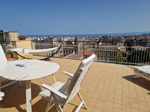 Terrazza sul tetto dell'Aparthotel Bentivoglio a Catania con vista panoramica sulla città e il mare, arredo bianco e lettini.