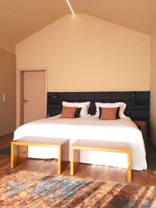 Quarto moderno no hotel Em Xisto em Góis com cabeceira preta, roupa branca, bancos de madeira e paredes terra