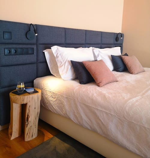 Quarto moderno do hotel Em Xisto com cabeceira estofada escura, roupa de cama branca, almofadas decorativas e mesa lateral de madeira