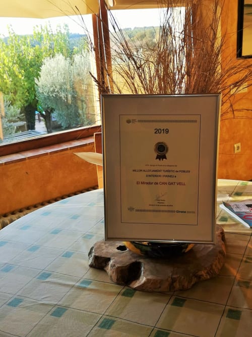 Placa de premio 2019 de El Mirador de Can Gat Vell, una casa rural en Girona, exhibida en interior con decoración de paja seca
