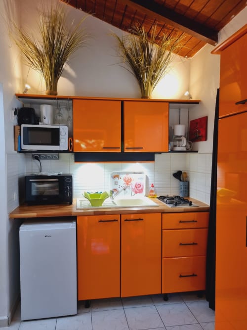 Bright orange and black kitchenette at Gites Kaladja studio in Port-Louis with microwave, stove, sink, refrigerator and