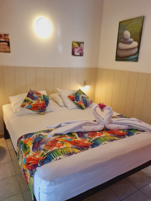Colorful tropical studio bedroom with decorated double bed, white pillows, and towel swans at Gites Kaladja, Port-Louis