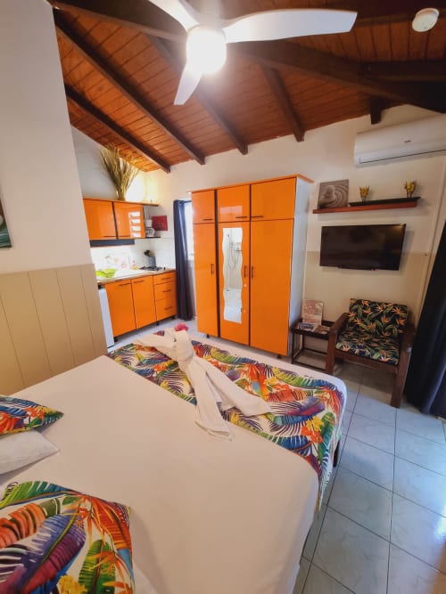 Bright studio apartment at Gites Kaladja with orange kitchenette, wooden ceiling, colorful bedding, and modern amenities in