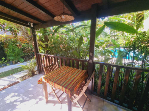Tropical studio terrace at Gites Kaladja with dining table, rattan pendant light, and lush garden views in Port-Louis,
