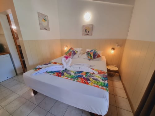 Colorful tropical studio bedroom at Gites Kaladja with white bed, warm lighting, and vibrant patterned bedding in Port-Louis,
