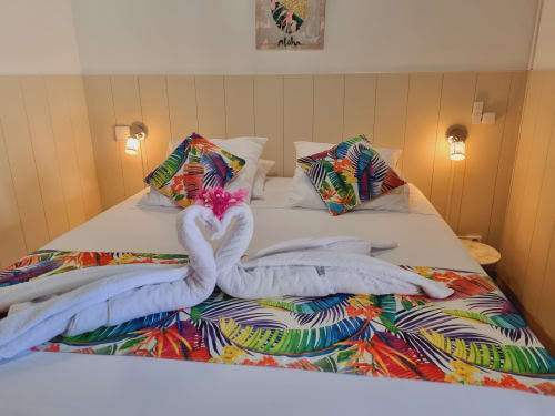 Tropical-themed studio bedroom at Gites Kaladja with colorful leaf pillows, white towel swans, and vibrant bedding in