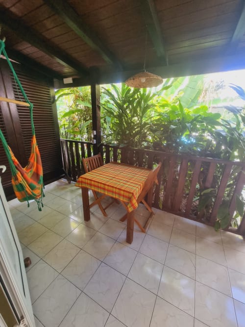 Covered outdoor dining area at Gites Kaladja with wooden table, colorful tablecloth, hanging hammock, and lush tropical