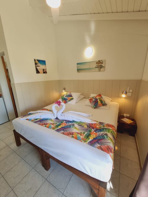 Bright studio bedroom at Gites Kaladja with two single beds, tropical décor, wooden headboard, and beach-themed wall art in