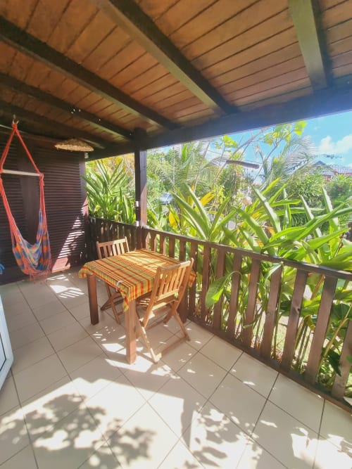 Sunny covered patio at Gites Kaladja with wooden dining table, red hammock, and lush tropical garden views in Port-Louis