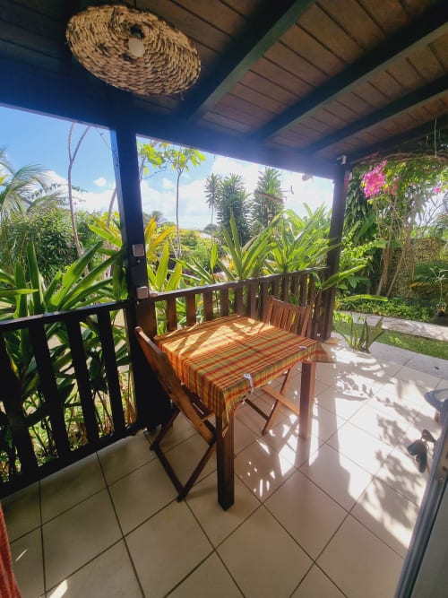 Covered outdoor dining area at Gites Kaladja with wooden table, tropical garden views, and comfortable seating in Port-Louis