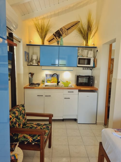 Compact kitchenette in Mendé studio at Gites Kaladja, Port-Louis, with white cabinets, wooden counter, microwave, and