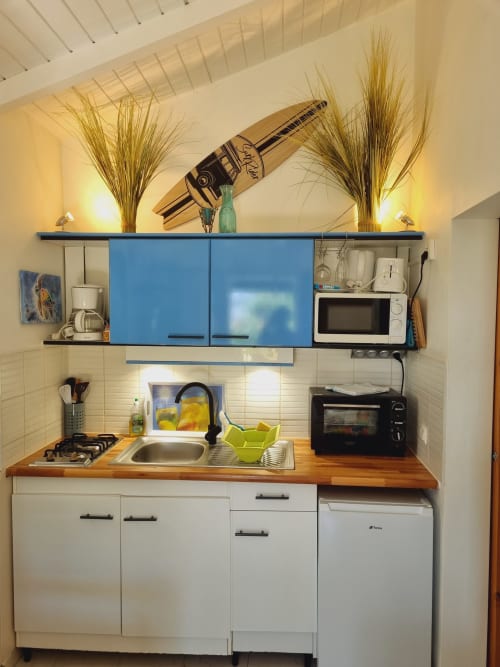 Compact studio kitchenette with blue cabinets, wooden countertop, sink, stove, and microwave at Gites Kaladja, Port-Louis