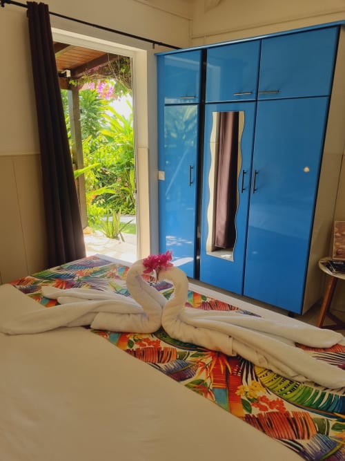 Bright bedroom at Gites Kaladja with towel swans, colorful bedding, blue wardrobe, and garden view through glass doors in