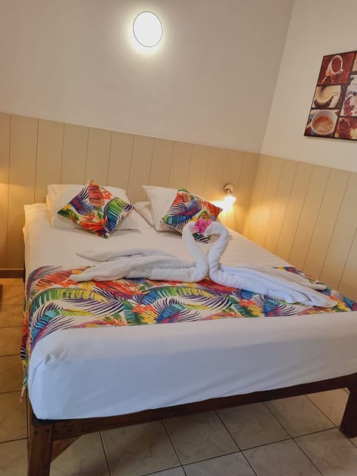 Colorful studio bedroom at Gites Kaladja with double bed, white pillows, tropical bedding, beige headboard, and modern