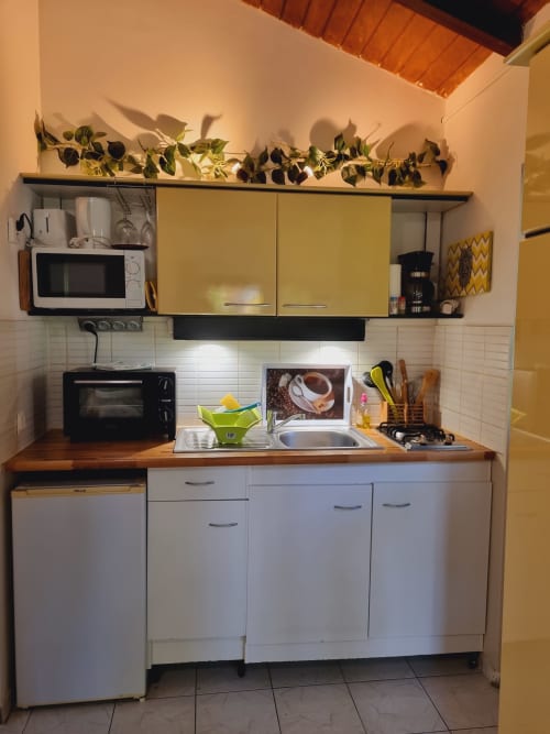 Compact kitchenette at Gites Kaladja studio in Port-Louis with white cabinets, wooden countertop, microwave, stove, and