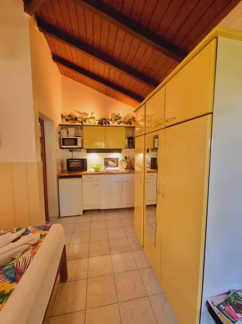 Bright yellow kitchenette in Toumblak studio at Gites Kaladja, Port-Louis with white cabinets and wooden ceiling beams